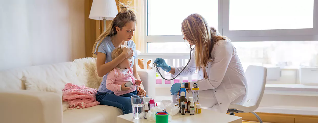 Doctor doing a health check up of a young girl sitting on mother’s lap